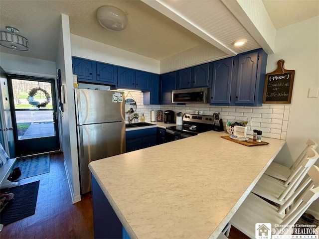 kitchen featuring a sink, blue cabinets, a peninsula, and appliances with stainless steel finishes