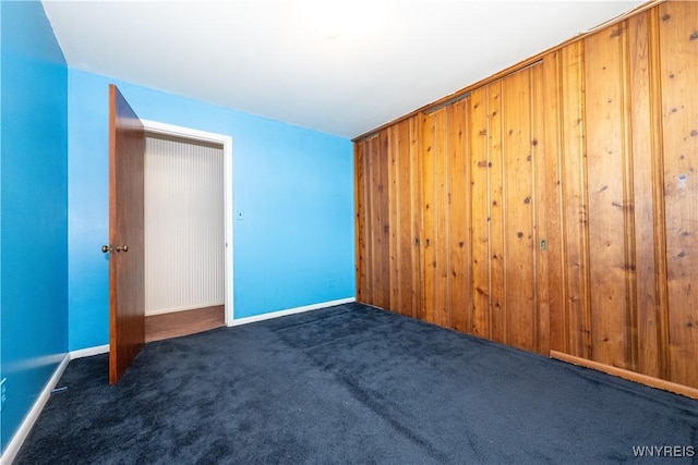 unfurnished bedroom with a closet, carpet flooring, baseboards, and wooden walls