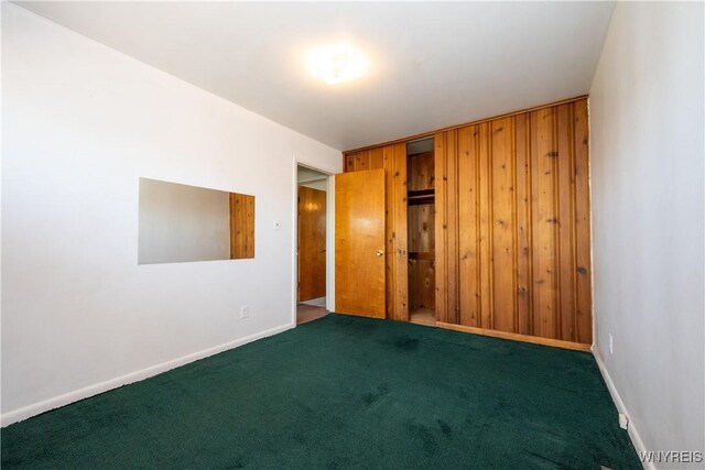 carpeted empty room with wooden walls and baseboards