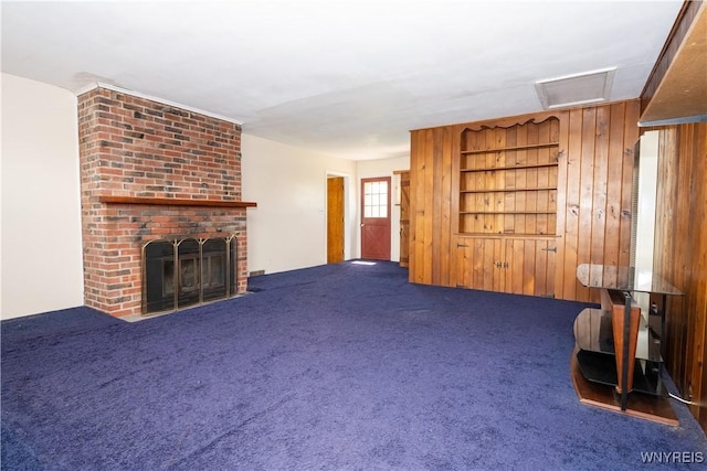 unfurnished living room with wood walls, a fireplace, dark colored carpet, and visible vents