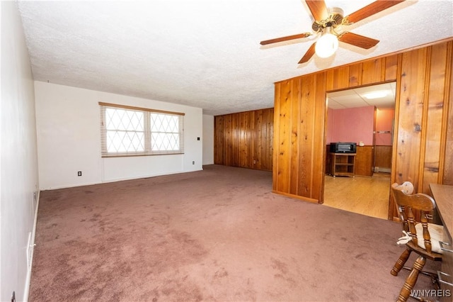 living room with wooden walls, ceiling fan, carpet, and a textured ceiling