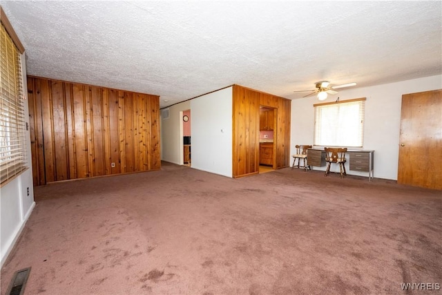 unfurnished living room featuring a textured ceiling, wood walls, carpet, a ceiling fan, and visible vents