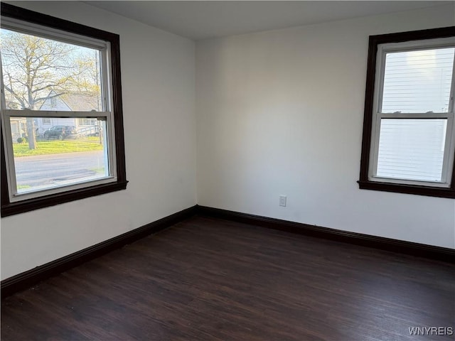 spare room featuring dark wood-style flooring, baseboards, and a healthy amount of sunlight