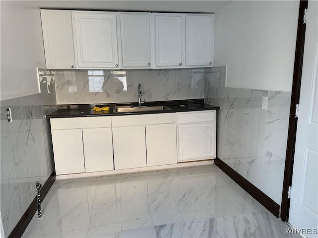 kitchen featuring white cabinetry, a sink, dark countertops, tile walls, and marble finish floor