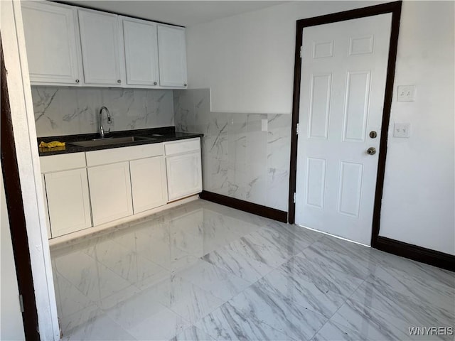 kitchen featuring dark countertops, marble finish floor, a sink, and white cabinetry