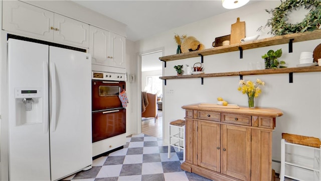 kitchen featuring open shelves, white refrigerator with ice dispenser, tile patterned floors, double wall oven, and white cabinetry