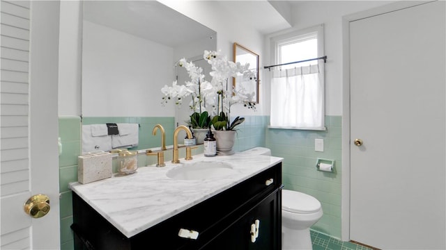 bathroom with vanity, toilet, tile walls, tile patterned floors, and a wainscoted wall