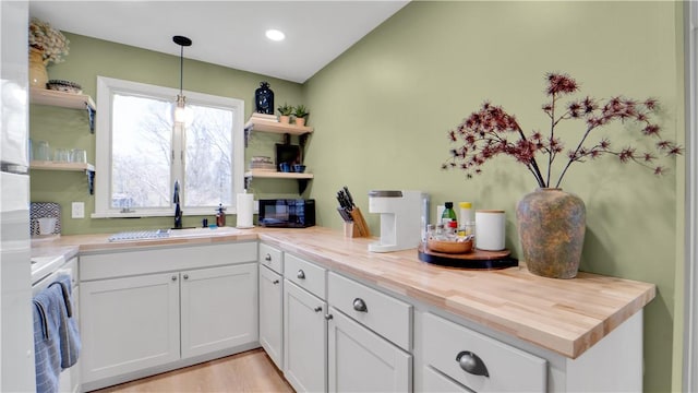 kitchen featuring open shelves, a sink, black microwave, and white cabinetry