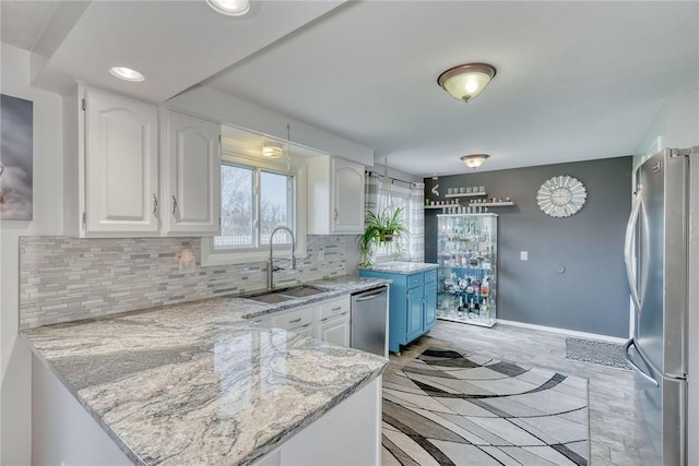 kitchen with appliances with stainless steel finishes, white cabinets, backsplash, a sink, and a peninsula