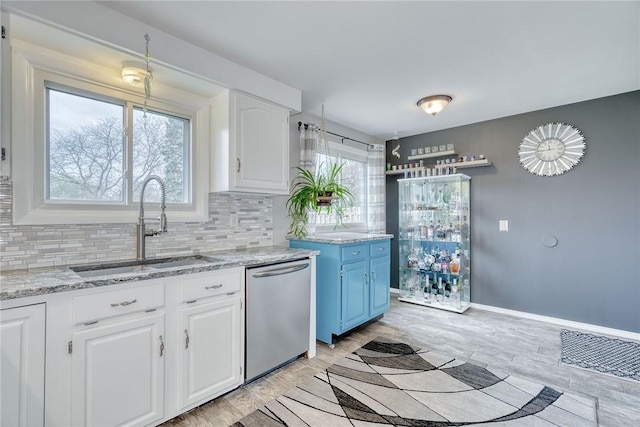 kitchen featuring tasteful backsplash, stainless steel dishwasher, white cabinets, a sink, and light stone countertops
