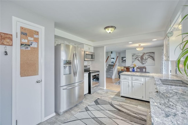 kitchen featuring light stone countertops, appliances with stainless steel finishes, white cabinets, a sink, and a peninsula