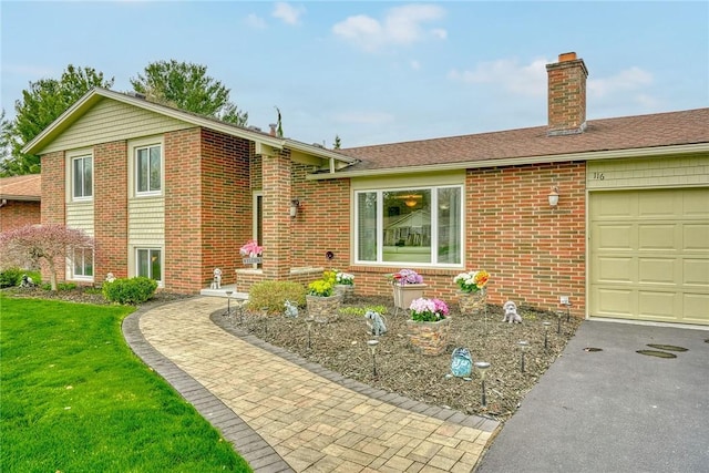 tri-level home featuring a chimney, brick siding, aphalt driveway, a garage, and a front yard