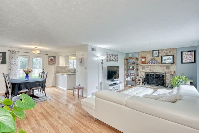living room featuring visible vents, a fireplace, a textured ceiling, and light wood-style flooring