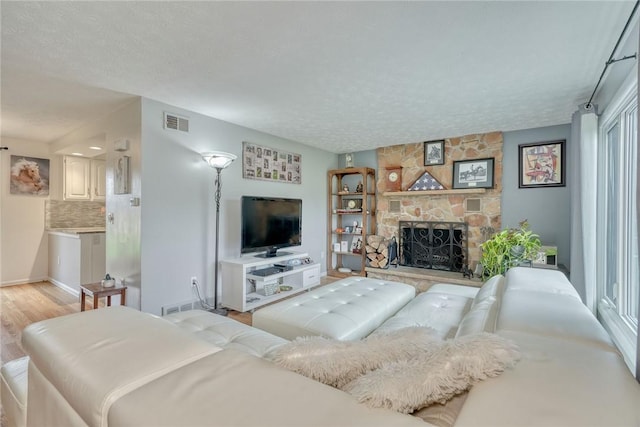 living area featuring visible vents, a fireplace, a textured ceiling, and light wood-style flooring