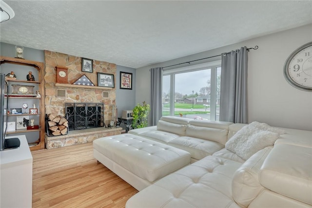 living room featuring a textured ceiling, wood finished floors, and a stone fireplace