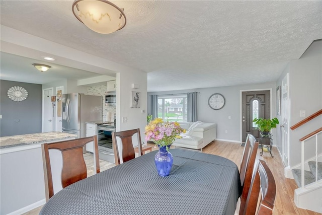 dining space featuring light wood finished floors, a textured ceiling, stairway, and baseboards