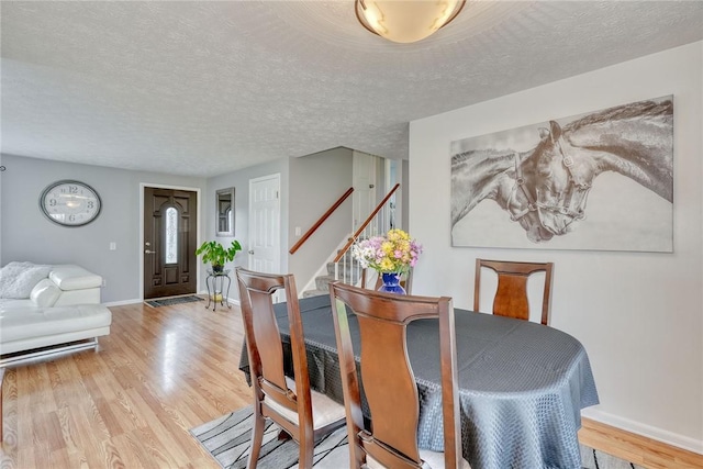 dining space with stairway, wood finished floors, a textured ceiling, and baseboards