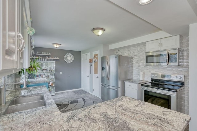kitchen featuring tasteful backsplash, light stone countertops, stainless steel appliances, a sink, and white cabinetry