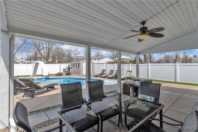 view of patio with an outdoor structure, ceiling fan, outdoor dining area, a fenced backyard, and a shed