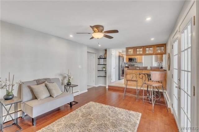 living room featuring wood finished floors, baseboards, a baseboard radiator, recessed lighting, and a ceiling fan