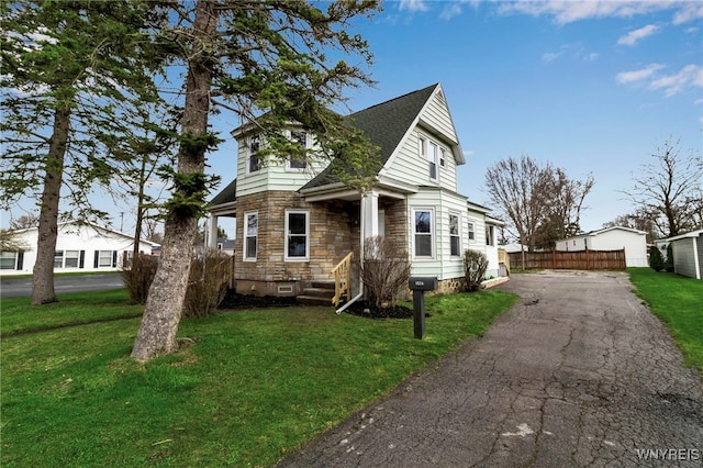 view of front of home with fence, driveway, a front yard, and stone siding