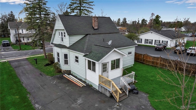 back of house featuring a shingled roof, a residential view, a yard, a chimney, and fence