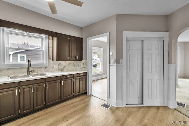 kitchen with a sink, dark brown cabinetry, a ceiling fan, visible vents, and arched walkways