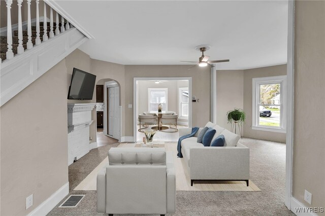 living room with carpet flooring, a fireplace, ceiling fan, visible vents, and arched walkways