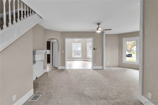 unfurnished living room with visible vents, arched walkways, ceiling fan, and carpet