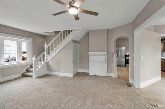 unfurnished living room with stairway, visible vents, a ceiling fan, and arched walkways