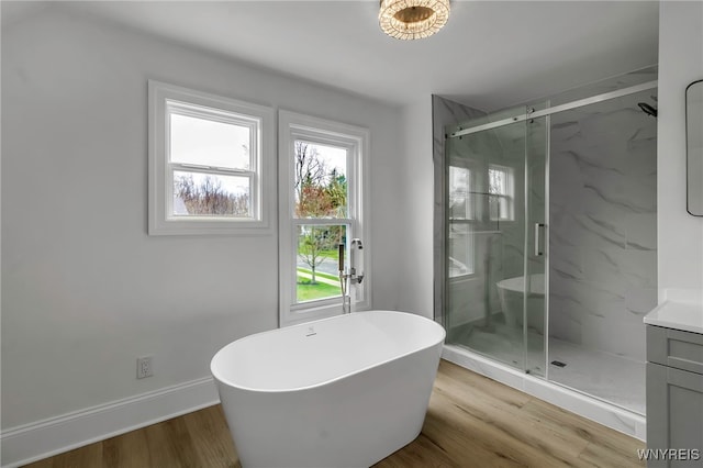 bathroom with a soaking tub, baseboards, a marble finish shower, wood finished floors, and vanity