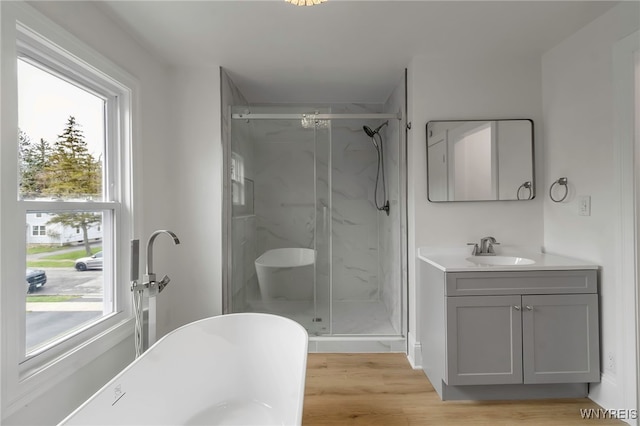 bathroom with a soaking tub, wood finished floors, vanity, and a marble finish shower