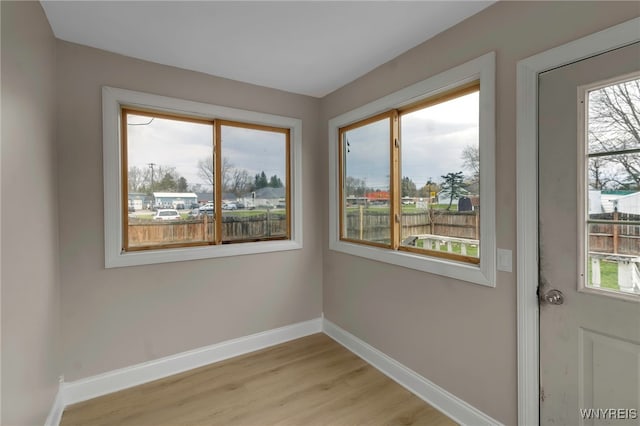 unfurnished room featuring light wood finished floors, plenty of natural light, and baseboards