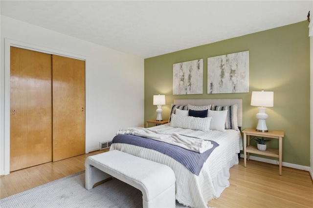 bedroom with baseboards, visible vents, light wood finished floors, and a closet