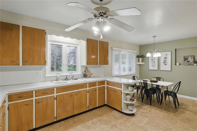 kitchen featuring light countertops, a peninsula, a sink, and ceiling fan with notable chandelier