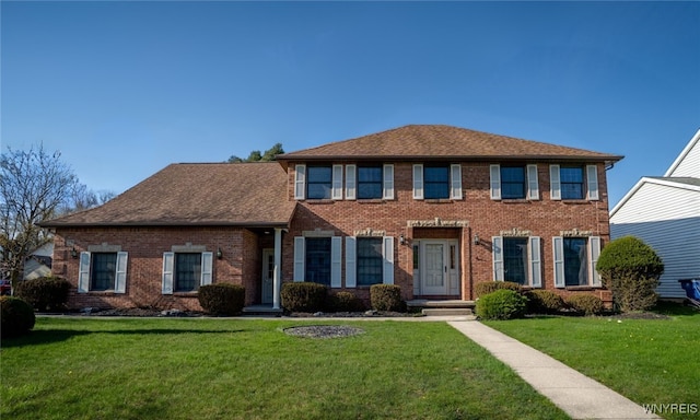 colonial-style house featuring roof with shingles, brick siding, and a front yard