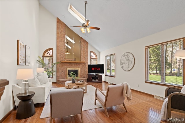living room featuring ceiling fan, a fireplace, wood-type flooring, high vaulted ceiling, and a skylight