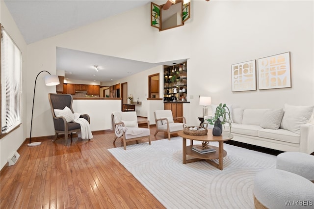 living room with light wood-style floors, high vaulted ceiling, baseboards, visible vents, and bar area