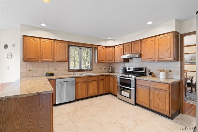 kitchen with brown cabinets, stainless steel appliances, a sink, and tasteful backsplash