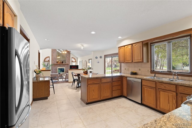 kitchen with a peninsula, a sink, backsplash, vaulted ceiling, and stainless steel appliances