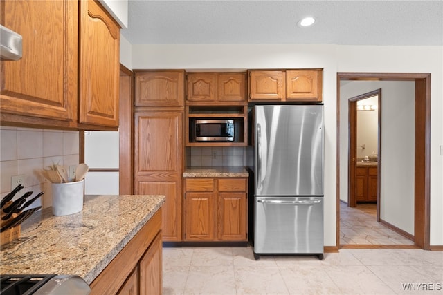 kitchen featuring backsplash, stainless steel appliances, light stone counters, and brown cabinetry