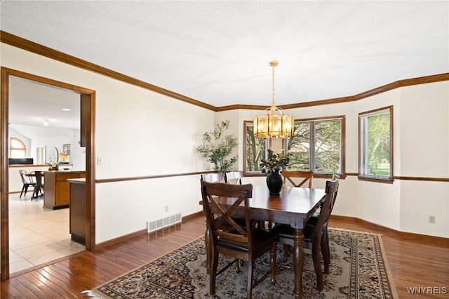 dining space with visible vents, crown molding, baseboards, light wood-type flooring, and a notable chandelier