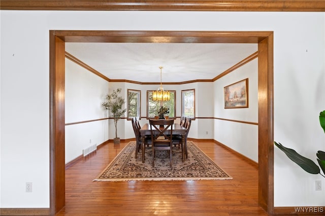 dining area featuring crown molding, visible vents, an inviting chandelier, and hardwood / wood-style flooring