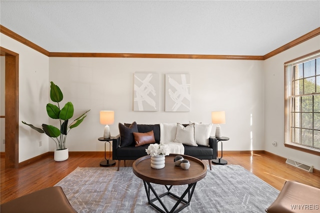living room featuring baseboards, ornamental molding, wood finished floors, and visible vents