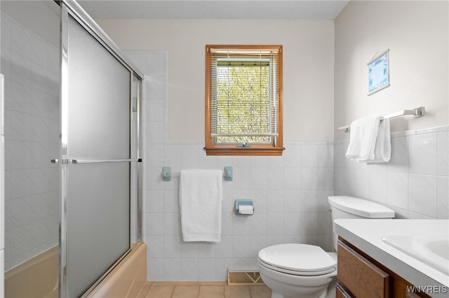 full bathroom featuring tile walls, tile patterned floors, vanity, combined bath / shower with glass door, and toilet