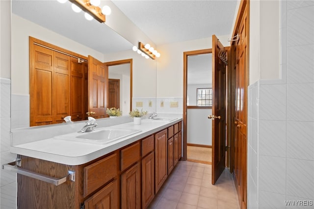 bathroom featuring double vanity, a sink, tile patterned floors, and tile walls