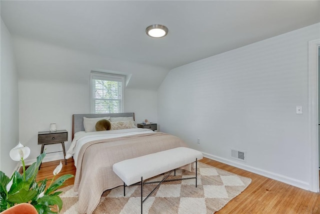 bedroom with baseboards, vaulted ceiling, light wood finished floors, and visible vents