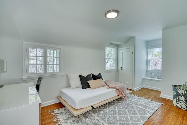 bedroom featuring baseboards, wood finished floors, vaulted ceiling, and multiple windows