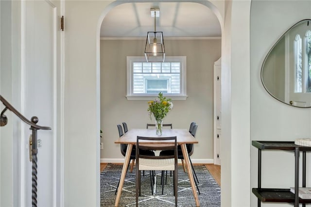 dining space featuring arched walkways, baseboards, ornamental molding, and wood finished floors
