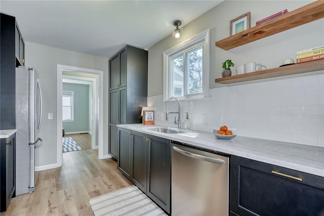 kitchen with decorative backsplash, light countertops, a sink, light wood-style flooring, and appliances with stainless steel finishes